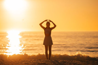 Rear view of woman standing at beach against sky during sunset