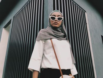 Portrait of woman wearing sunglasses and hijab while standing against wall