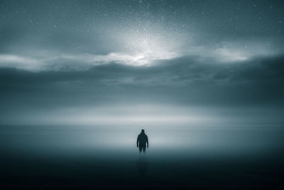 Rear view of silhouette person standing in sea against sky