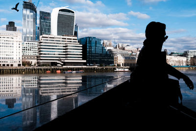 Silhouette of man and  bird against sky and modern buildings in city 