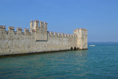 Built structure by sea against clear blue sky