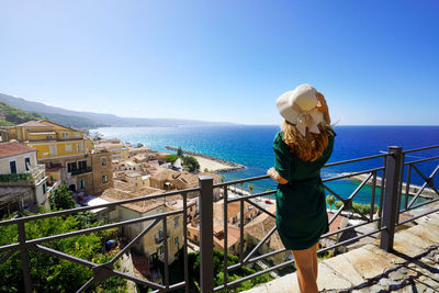 Tourist woman with straw hat enjoying view of pizzo village from terrace in calabria, italy.