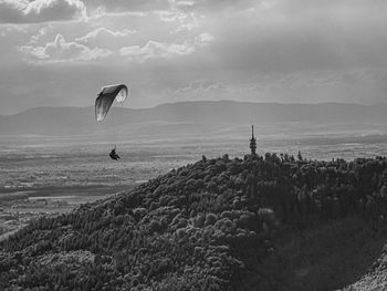 Person paragliding over mountain against sky