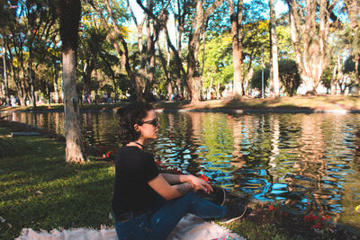 Man sitting by tree trunk by lake