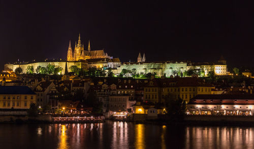 Illuminated buildings by river against sky at night