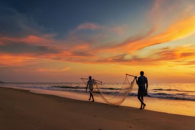 Silhouette people on beach against sky during sunset