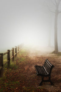 Empty bench by railing in foggy weather