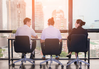 Rear view of business people sitting on chairs at table by window