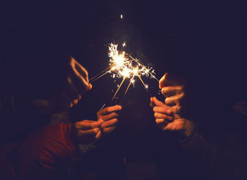 Close-up of people holding lit sparklers at night