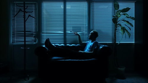 Man relaxing on sofa against window blinds