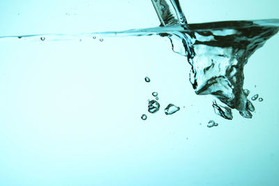 Close-up of drop falling on water against blue background