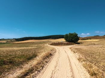 Dirt road amidst field against clear blue sky