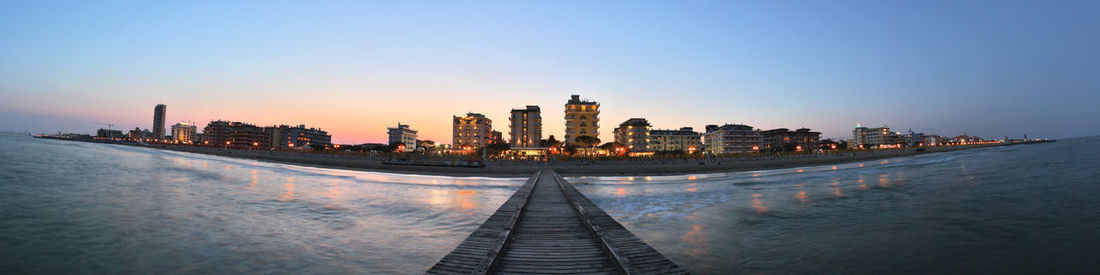 Beach promenade in italy, panoramic view of buildings against sky during sunset