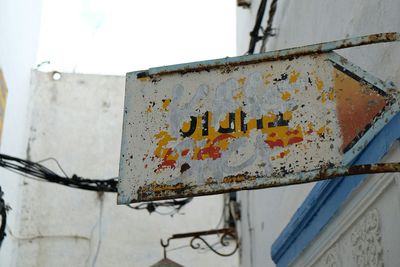 Low angle view of damaged sign board mounted on building