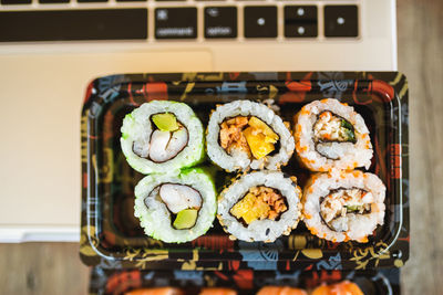 Top view of laptop and tasty sushi rolls wit with wine at wooden table