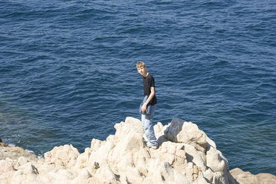 Full length of man standing on cliff by sea during sunny day