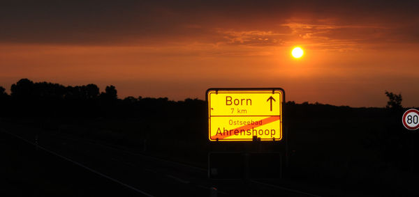 Information sign on railroad tracks against sky during sunset