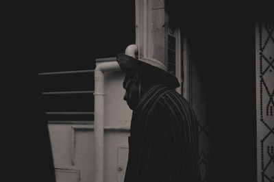 Side view of young man standing against window