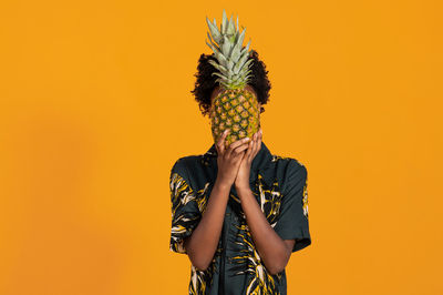 Young african american woman with short hair dressed in a summer shirt posing with pineapple