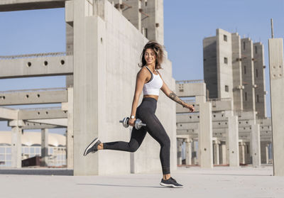 Young woman holding dumbbell while exercising in city