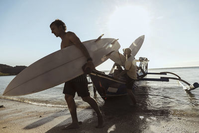 Adult men carrying surfboards while unloading vessel