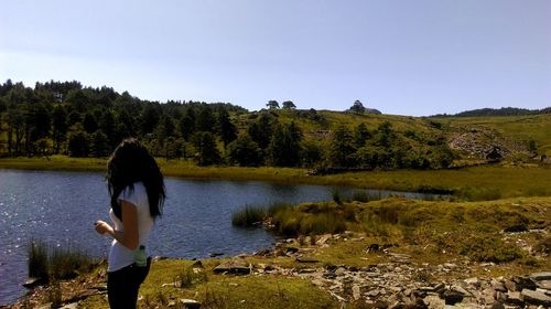 Rear view of woman standing by lake against clear sky