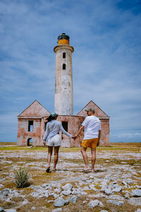 Rear view of people walking by lighthouse against sky