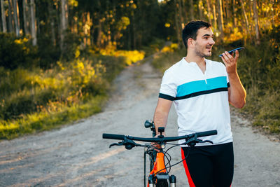 Smiling young man with cell phone pushing bicycle