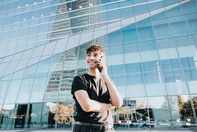 Low angle view of young man standing against modern buildings