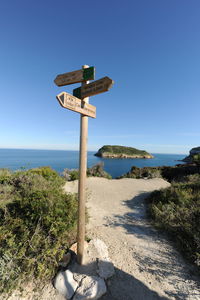 Sign board by sea against clear blue sky