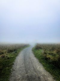 Dirt road amidst field against sky