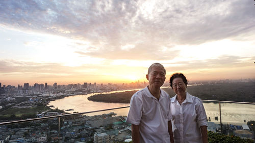 Portrait of smiling man standing on city against sky during sunset