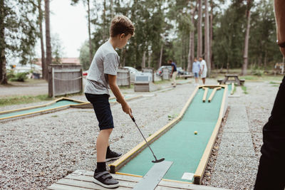 Full length of boy playing miniature golf in backyard against tree