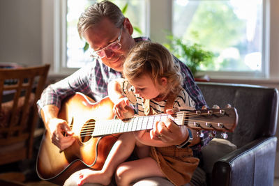 Grandfather teaching guitar to granddaughter at home