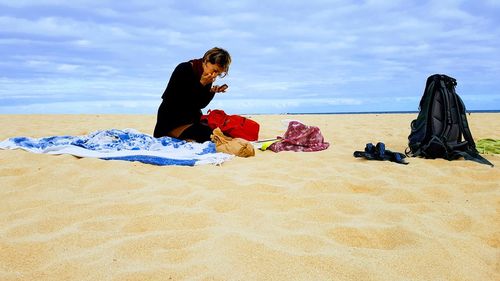 Woman sitting on beach by sea against sky