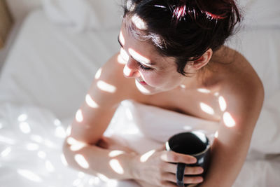 Woman sitting on bed while holding coffee cup at home
