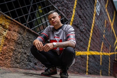 Portrait of young man sitting against wall