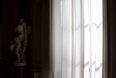 Statue on table by covered window