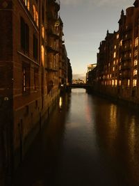 Canal amidst buildings in city at sunset