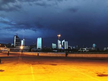 Illuminated street by buildings against sky at night