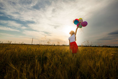 Woman holding balloons on field against sky