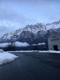 Snow covered road by snowcapped mountains against sky