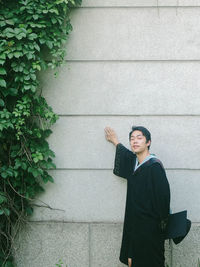 Young man looking away while standing against wall