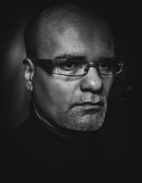 Close-up portrait of man wearing eyeglasses against black background