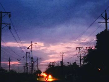 Silhouette electricity pylons against sky at sunset