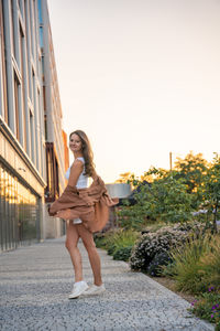 Full length of young woman standing on footpath