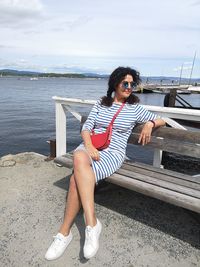 Young woman sitting by sea against sky