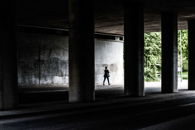 Rear view of silhouette woman walking under bridge