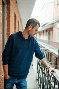 Man looking away while standing on railing against building