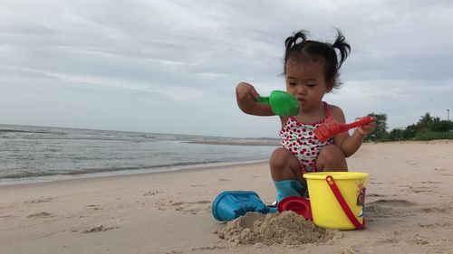 Cute girl playing on sand at beach against sky